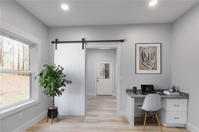 home office featuring light wood-type flooring, plenty of natural light, built in desk, and a barn door