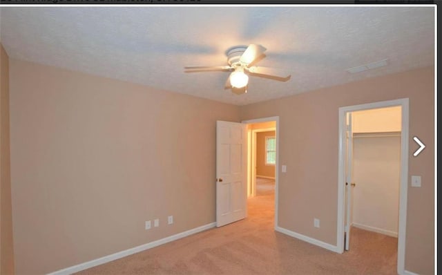 unfurnished bedroom featuring a walk in closet, light colored carpet, a ceiling fan, a textured ceiling, and baseboards