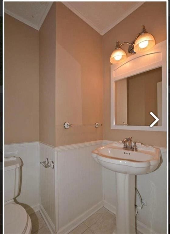 half bathroom featuring toilet, tile patterned floors, ornamental molding, and wainscoting