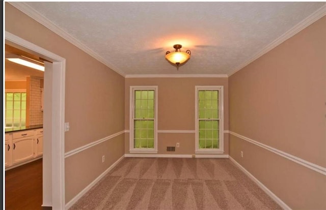 carpeted empty room with a textured ceiling, ornamental molding, visible vents, and baseboards