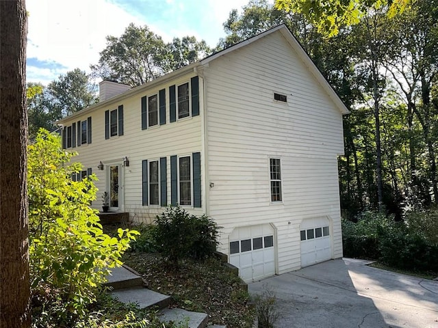 view of property exterior with a garage, concrete driveway, and a chimney