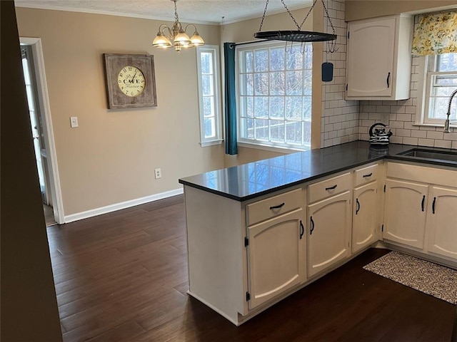 kitchen featuring dark wood finished floors, dark countertops, white cabinetry, a sink, and a peninsula