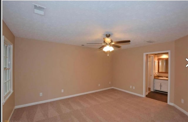 unfurnished bedroom with baseboards, a textured ceiling, ensuite bathroom, and light colored carpet