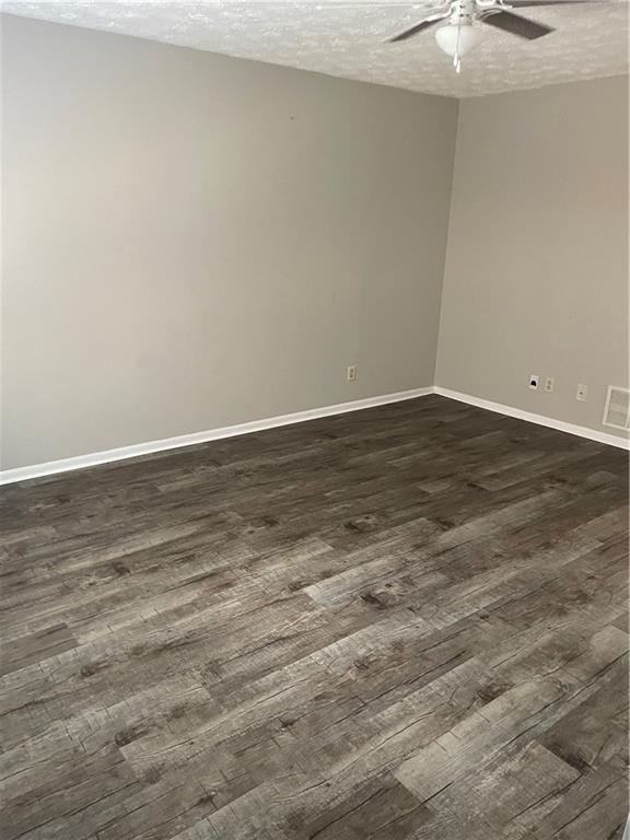 empty room with a textured ceiling, ceiling fan, and dark wood-type flooring