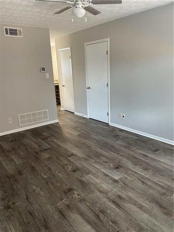 empty room with ceiling fan, dark hardwood / wood-style floors, and a textured ceiling