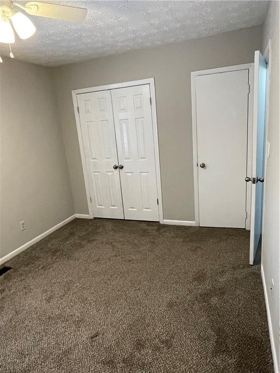 unfurnished bedroom featuring ceiling fan, dark carpet, a textured ceiling, and a closet