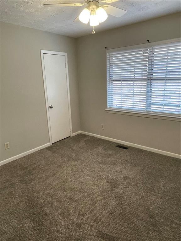 spare room featuring ceiling fan, dark carpet, and a textured ceiling