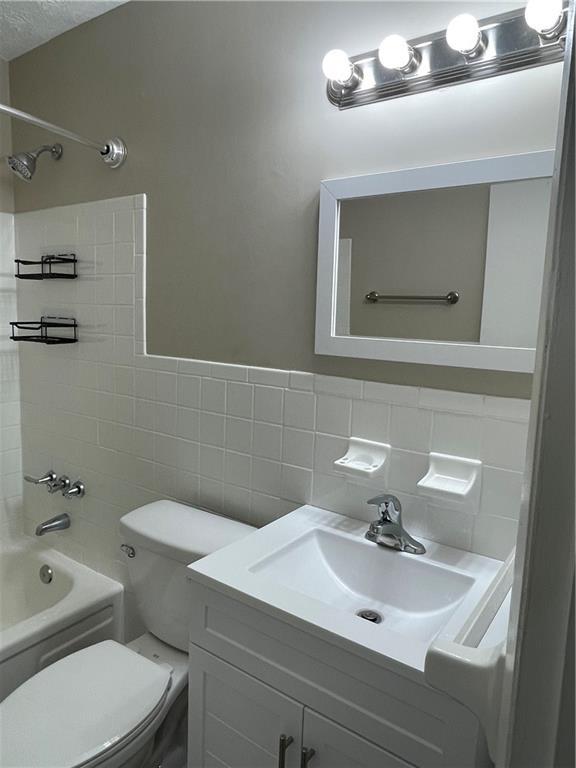 full bathroom featuring backsplash, tiled shower / bath, vanity, tile walls, and toilet