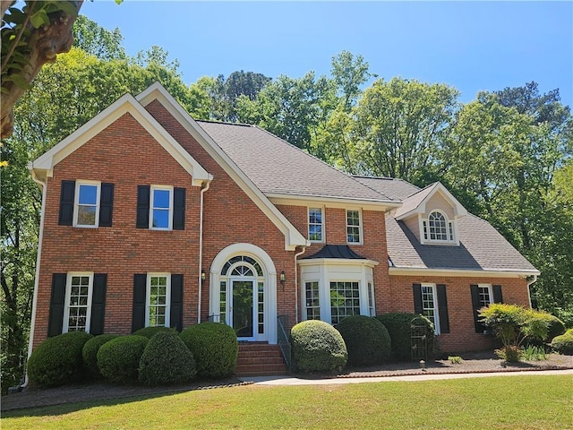 view of front of property with brick siding, a front yard, and roof with shingles