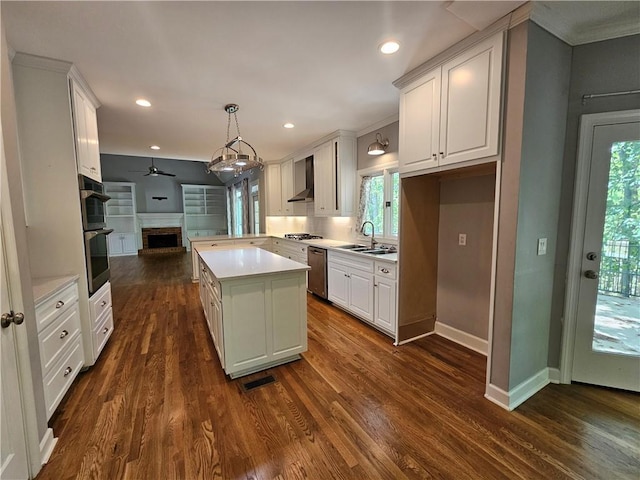 kitchen with stainless steel appliances, a sink, open floor plan, wall chimney range hood, and light countertops