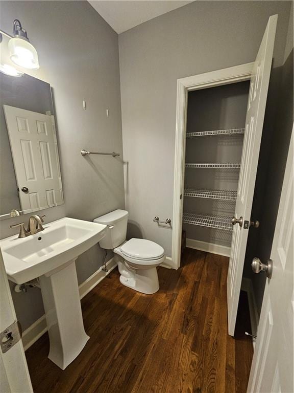 half bath with baseboards, wood finished floors, and toilet