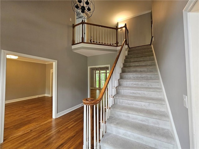 staircase with baseboards, a towering ceiling, a chandelier, and wood finished floors