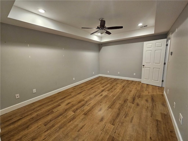 empty room featuring a raised ceiling, wood finished floors, a ceiling fan, and baseboards
