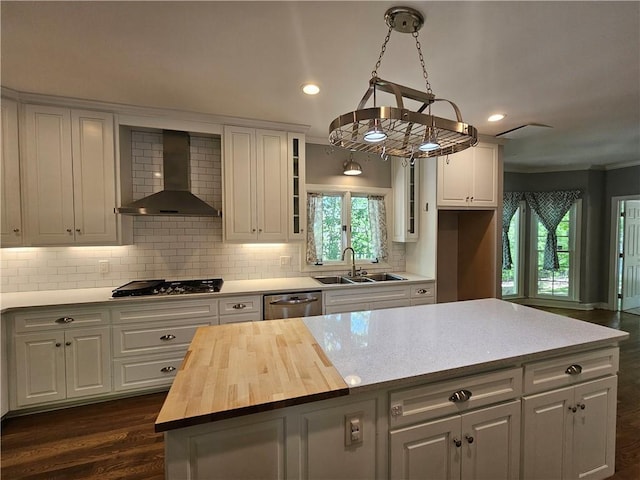 kitchen featuring gas cooktop, stainless steel dishwasher, a sink, wall chimney range hood, and wood counters