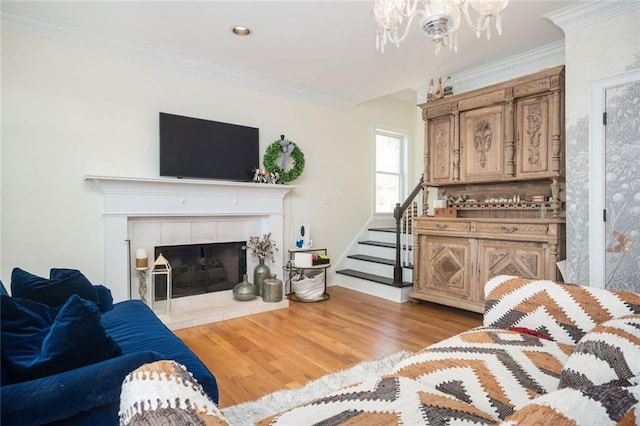 living area featuring crown molding, a tiled fireplace, a chandelier, light wood-type flooring, and stairs