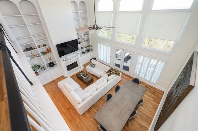 living area with a ceiling fan, a towering ceiling, built in features, and wood finished floors