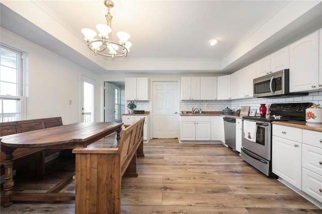 kitchen with decorative backsplash, appliances with stainless steel finishes, a tray ceiling, crown molding, and light wood-type flooring