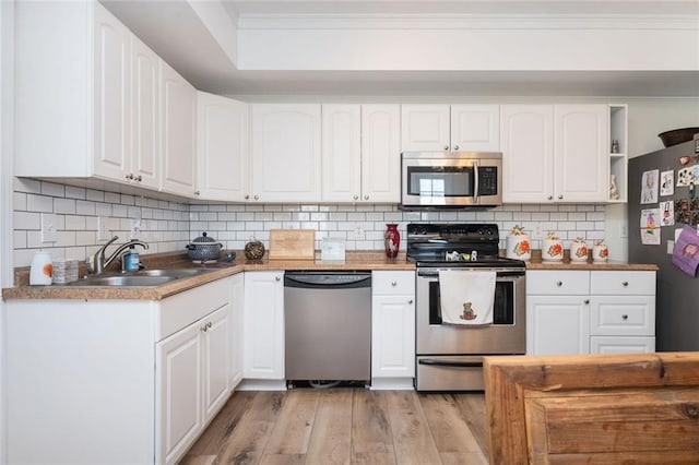 kitchen with backsplash, light wood-style flooring, appliances with stainless steel finishes, white cabinetry, and a sink