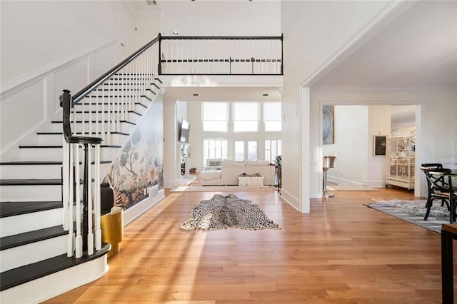 entryway featuring a towering ceiling, light wood-style flooring, stairs, and ornamental molding