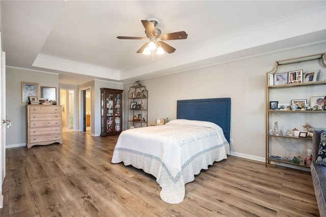 bedroom featuring wood finished floors, a ceiling fan, baseboards, a raised ceiling, and crown molding