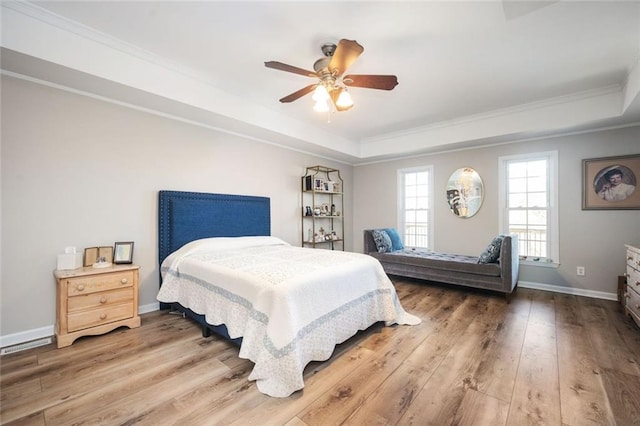 bedroom featuring wood-type flooring, baseboards, a raised ceiling, and crown molding