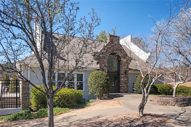 view of front of house with driveway, a shingled roof, a chimney, and stucco siding