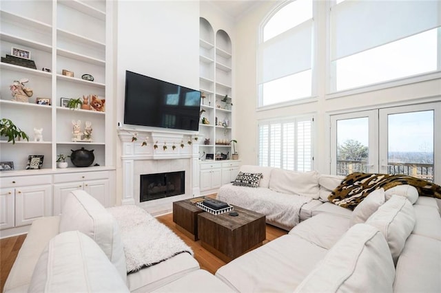 living area featuring a towering ceiling, built in shelves, wood finished floors, and a tile fireplace