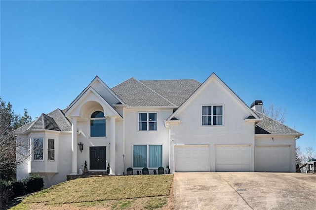 view of front of property with an attached garage, driveway, stucco siding, a front lawn, and a chimney