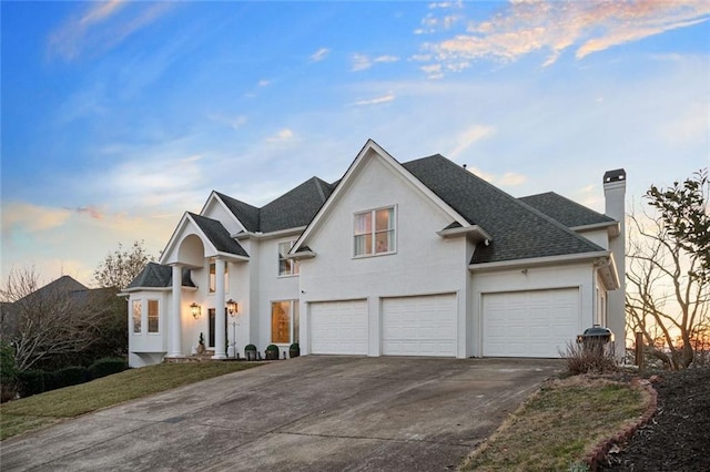 view of front of home with an attached garage, a shingled roof, concrete driveway, stucco siding, and a chimney