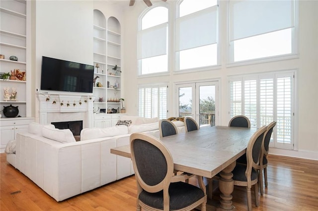 dining area featuring built in shelves, light wood finished floors, a high ceiling, a tiled fireplace, and baseboards