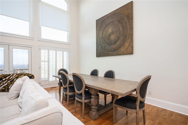 dining area featuring light wood finished floors, a high ceiling, and baseboards