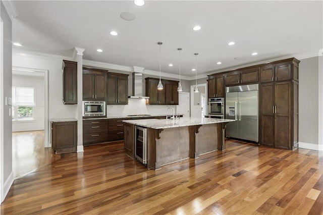 kitchen with built in appliances, wine cooler, wall chimney exhaust hood, dark wood-style floors, and recessed lighting
