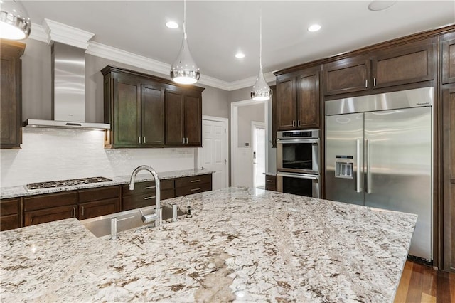 kitchen with stainless steel appliances, wall chimney range hood, a sink, ornamental molding, and dark brown cabinets