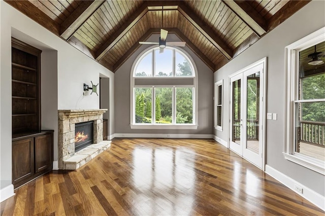 unfurnished living room with wooden ceiling, ceiling fan, a stone fireplace, wood finished floors, and beam ceiling