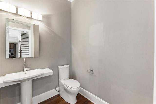 half bath featuring baseboards, toilet, and wood finished floors