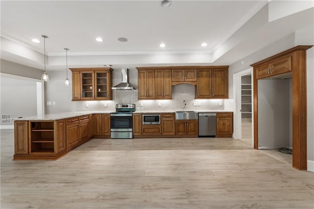 kitchen featuring stainless steel appliances, wall chimney range hood, a sink, brown cabinets, and a peninsula
