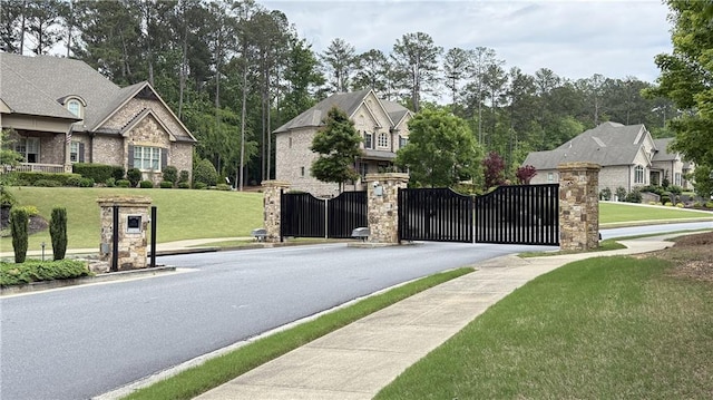 view of asphalt road featuring sidewalks, a gate, curbs, a gated entry, and a residential view