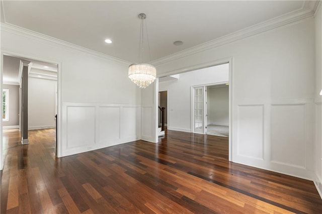 unfurnished dining area featuring a decorative wall, a chandelier, crown molding, dark wood-type flooring, and wainscoting