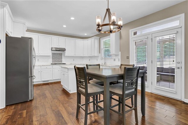 kitchen with dark hardwood / wood-style floors, stainless steel refrigerator, pendant lighting, white cabinetry, and backsplash