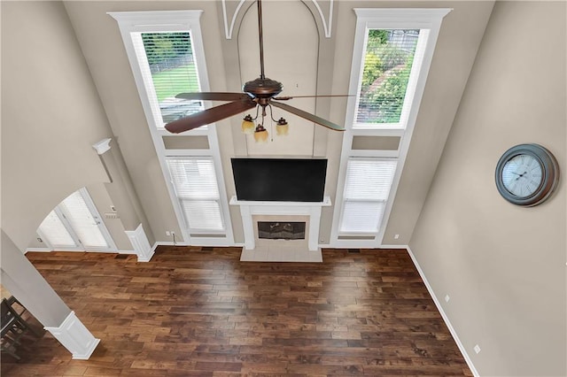 unfurnished living room with a towering ceiling, a tiled fireplace, dark hardwood / wood-style flooring, and ceiling fan