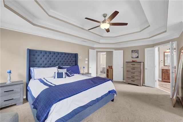 carpeted bedroom with a raised ceiling, ceiling fan, ornamental molding, and ensuite bath