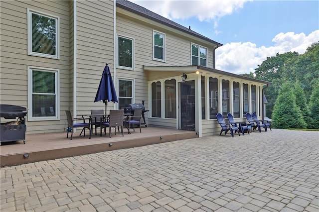 rear view of property featuring a sunroom, a deck, and a patio area