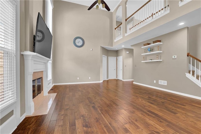 unfurnished living room with ceiling fan, a fireplace, hardwood / wood-style floors, and a high ceiling