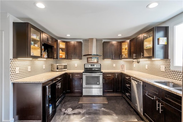 kitchen featuring appliances with stainless steel finishes, backsplash, light stone counters, and wall chimney range hood