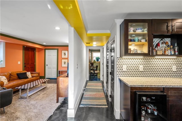 bar with wine cooler, light stone counters, backsplash, crown molding, and dark brown cabinets