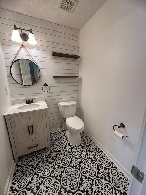 1732 Wyntercreek Ln, Hoschton, GA 30548 - half bathroom featuring toilet, wood walls, vanity, a textured ceiling, and visible vents