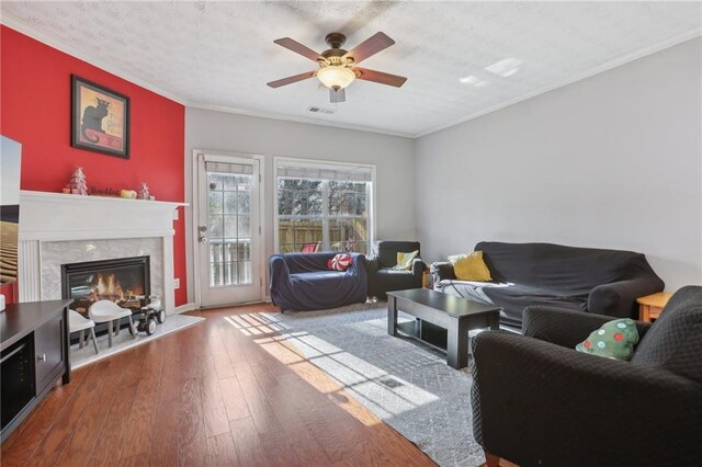 living room featuring hardwood / wood-style flooring, ceiling fan, a premium fireplace, ornamental molding, and a textured ceiling