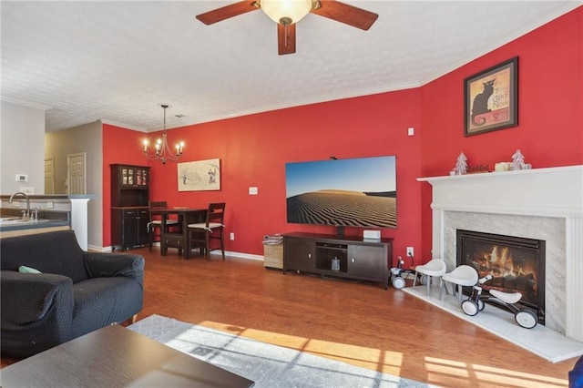 living room with sink, hardwood / wood-style flooring, a fireplace, ceiling fan with notable chandelier, and ornamental molding