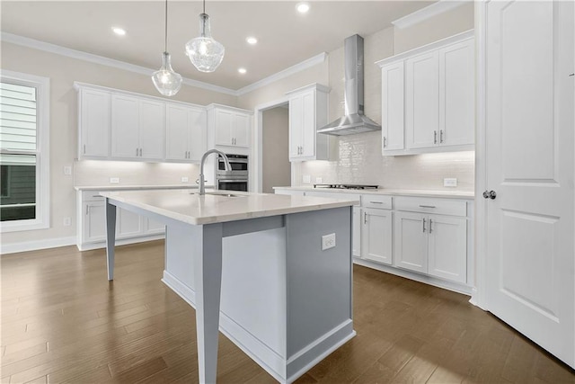 636 Silva St, Cumming, GA 30040 - kitchen featuring wall chimney exhaust hood, a sink, a center island with sink, light countertops, and crown molding