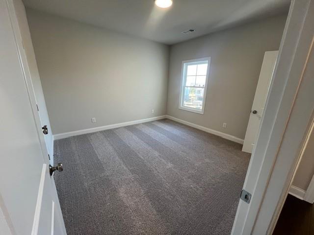 empty room with dark colored carpet, baseboards, and visible vents